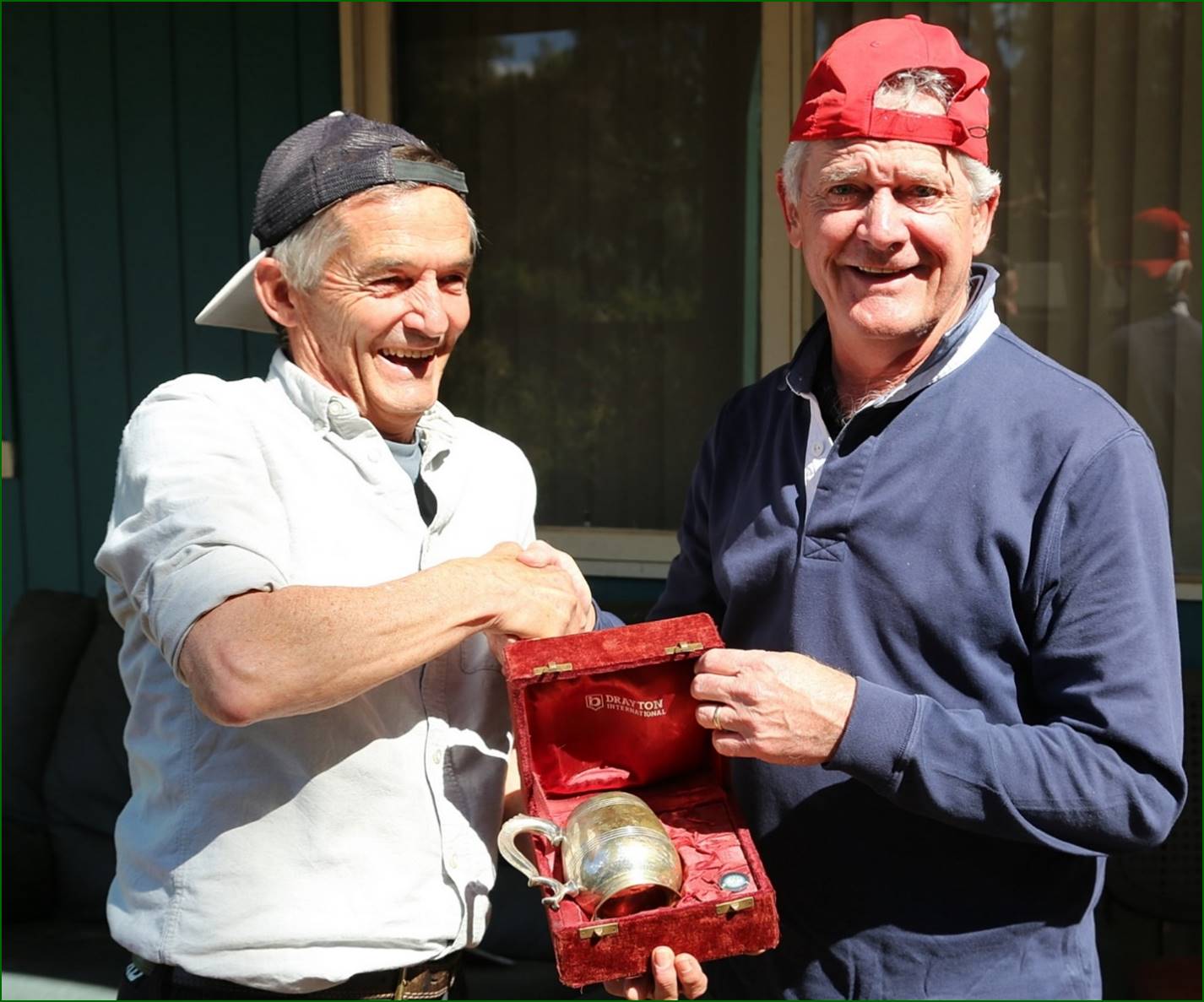 Two men holding a box with a silver object

Description automatically generated