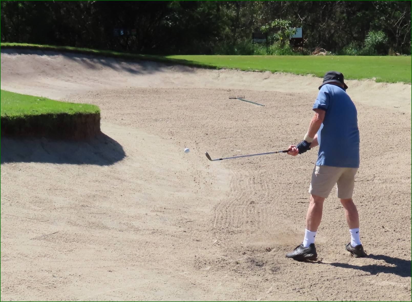 A person playing golf on a sand bunker

Description automatically generated