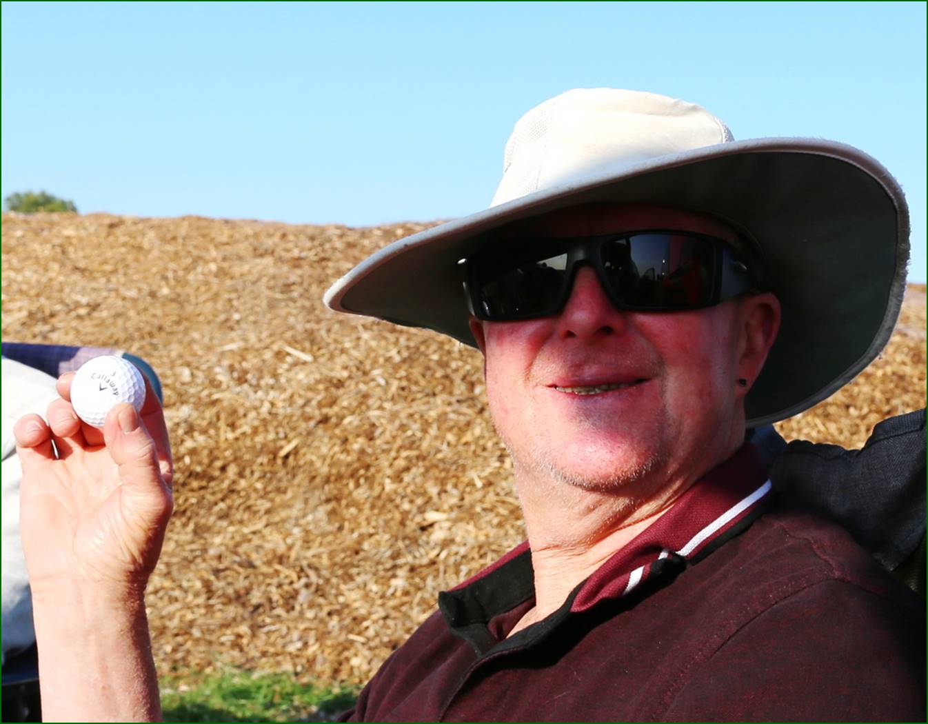 A person wearing a hat and sunglasses holding a golf ball

Description automatically generated